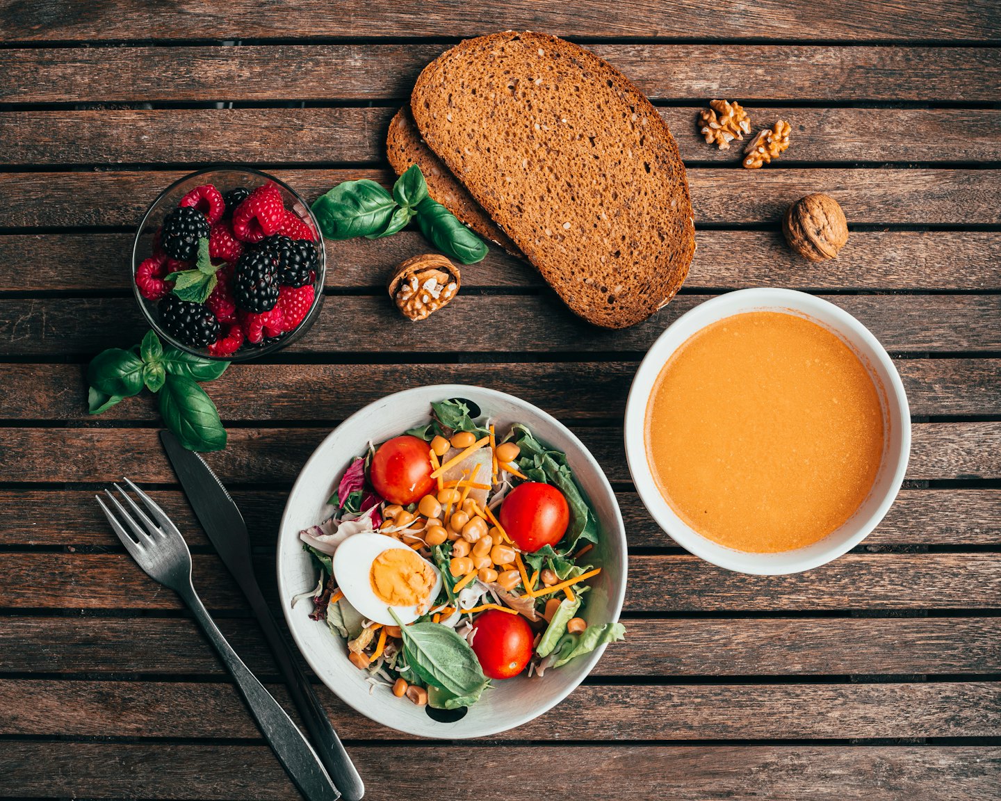 Gesunder Salat, Suppe, Brot und Beeren auf einem Holztisch.