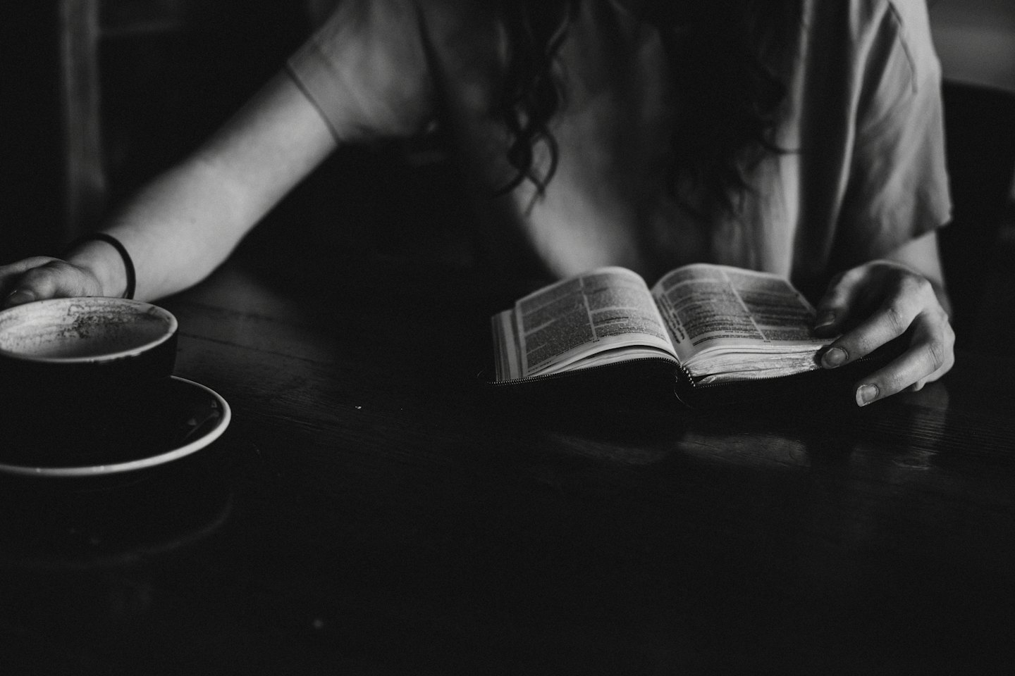 Frau liest ein Buch am Tisch mit Kaffee.