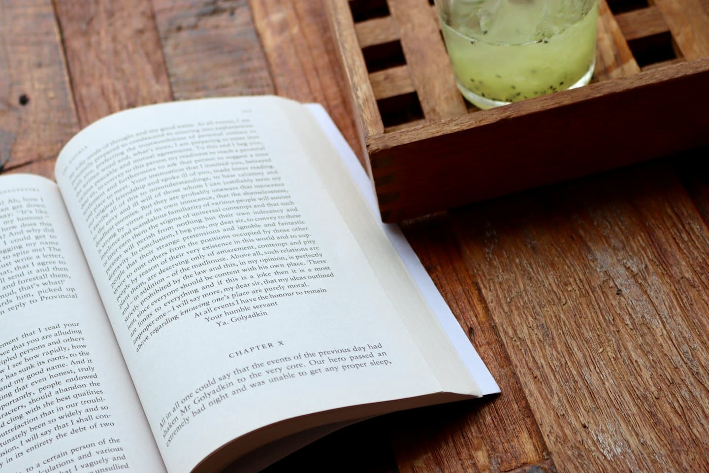 Ein aufgeschlagenes Buch und ein grünes Getränk mit Eis auf einem Tisch.